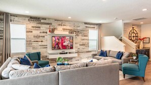 A modern living room with a grey sectional sofa, a teal armchair, and a flat-screen TV mounted on a wooden wall. - Ultimate 5 Star Villa with Private Pool on Encore Resort at Reunion, Orlando Villa 4391 (Orlando)