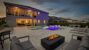A modern outdoor pool area with a fire feature, lounge chairs, and a two-story building with illuminated windows. - Ultimate 5 Star Villa with Private Pool on Encore Resort at Reunion, Orlando Villa 4391 (Orlando)