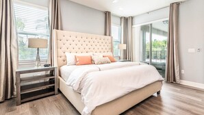 A bedroom with a large bed, a nightstand, a lamp, and a view of the outdoors through a large window. - Ultimate 5 Star Villa with Private Pool on Encore Resort at Reunion, Orlando Villa 4391 (Orlando)