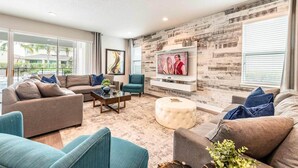 A modern living room with a sectional sofa, a round ottoman, a coffee table, and a television mounted on a wooden wall. - Ultimate 5 Star Villa with Private Pool on Encore Resort at Reunion, Orlando Villa 4391 (Orlando)