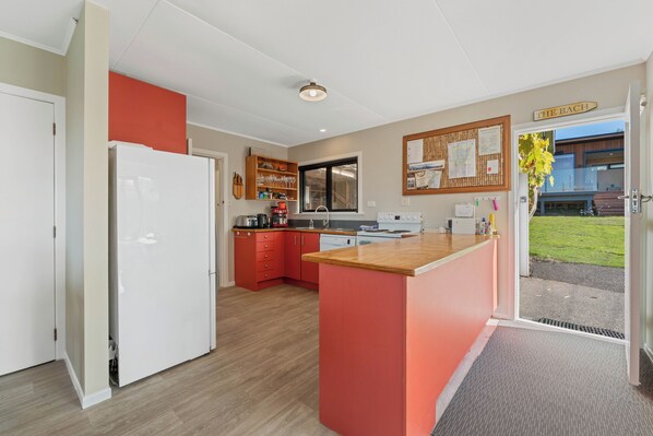 A modern kitchen with a central island, red cabinetry, and a view of the outside. - Henley - Omori Holiday Home (Omori)