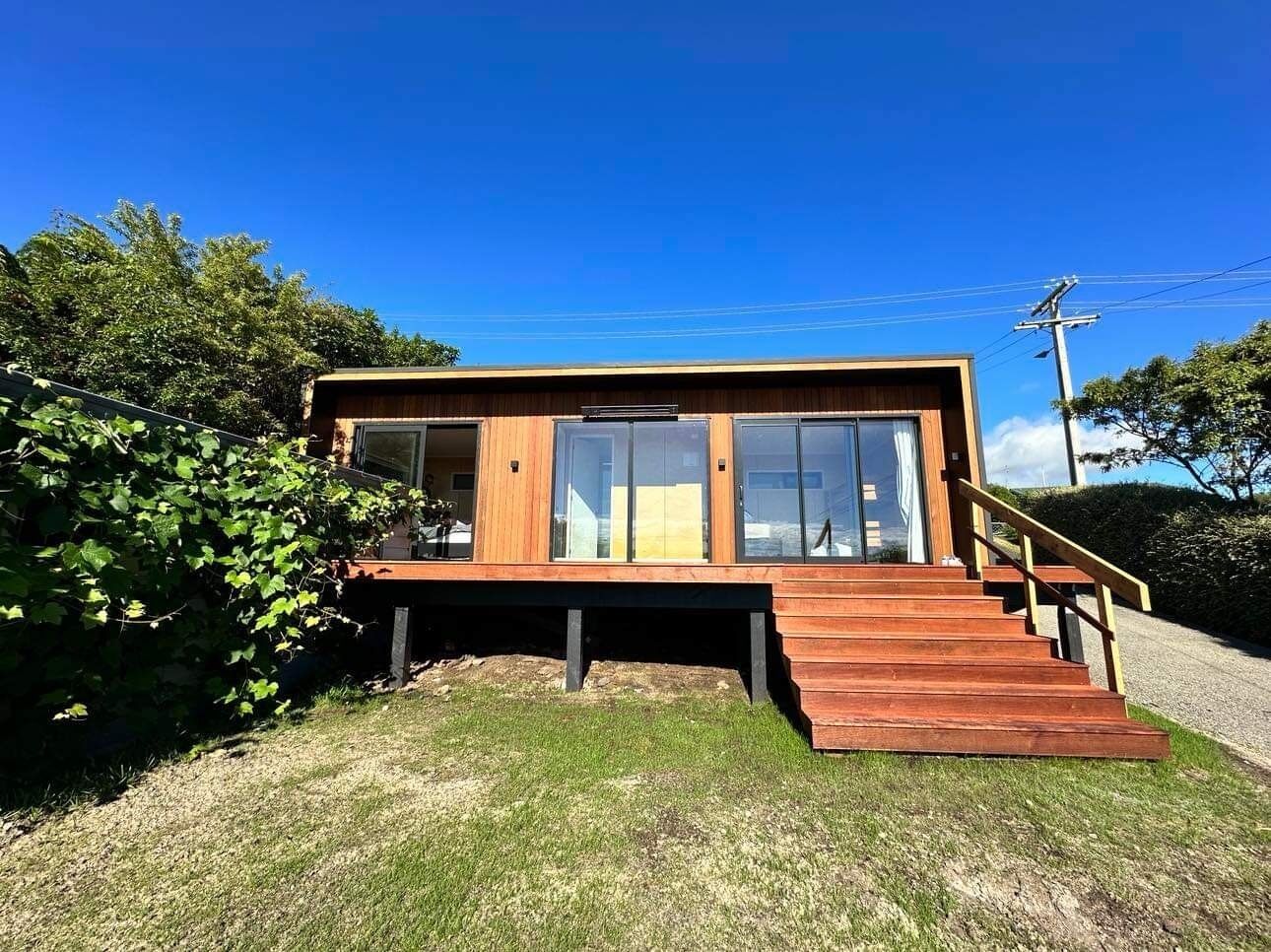 Una casa moderna de madera con amplios ventanales y una escalera de madera que lleva a una terraza.