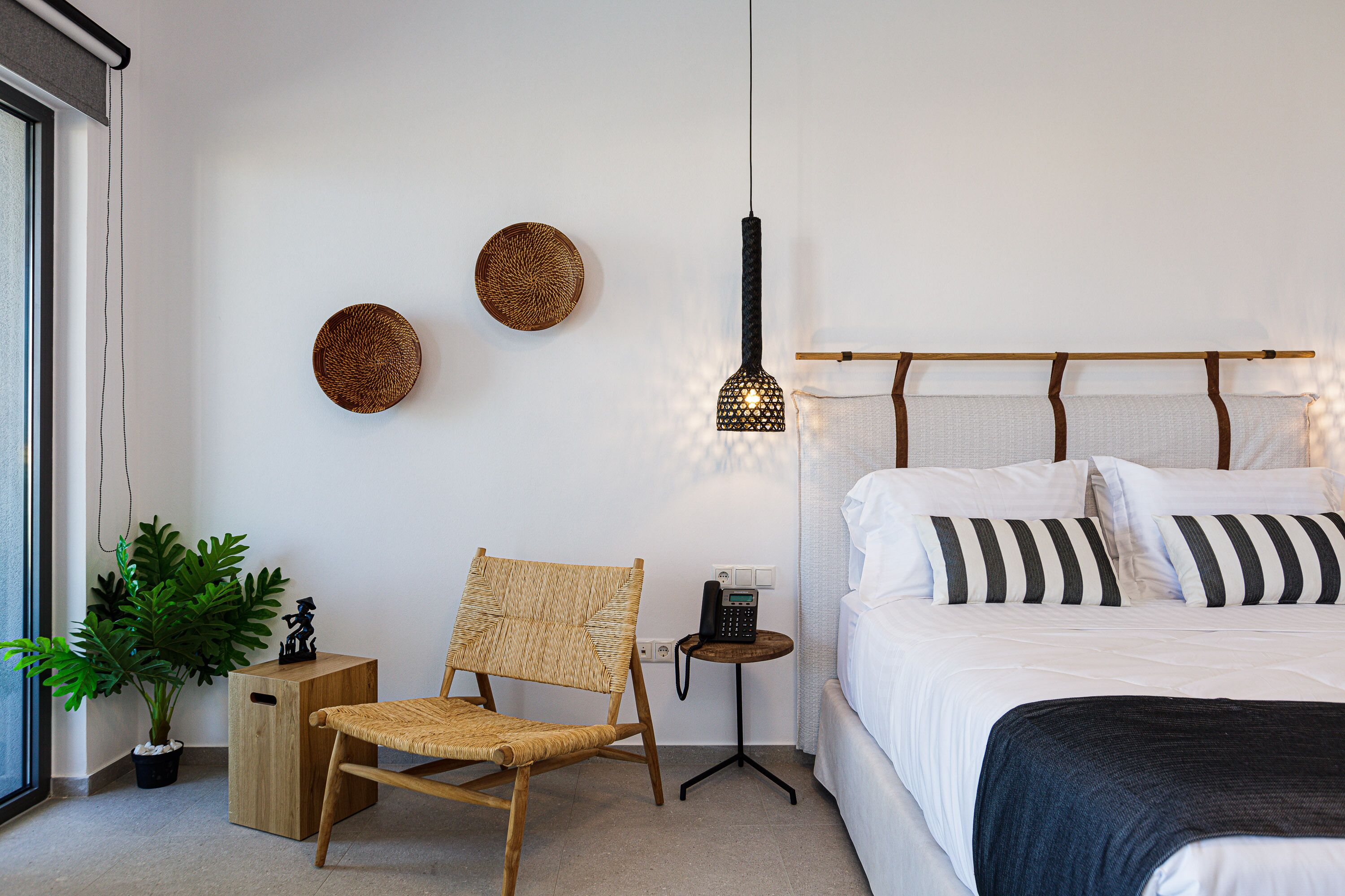 Ein modernes Schlafzimmer mit Bett, Sessel, Nachttisch, Wandlampe und einer Topfpflanze.