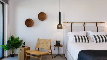 Ein modernes Schlafzimmer mit Bett, Sessel, Nachttisch, Wandlampe und einer Topfpflanze.