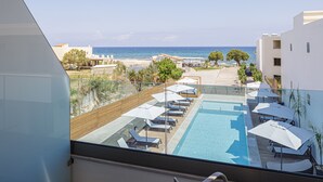 Una piscina en la azotea con sillas de descanso y sombrillas, con vistas a una playa y al mar.