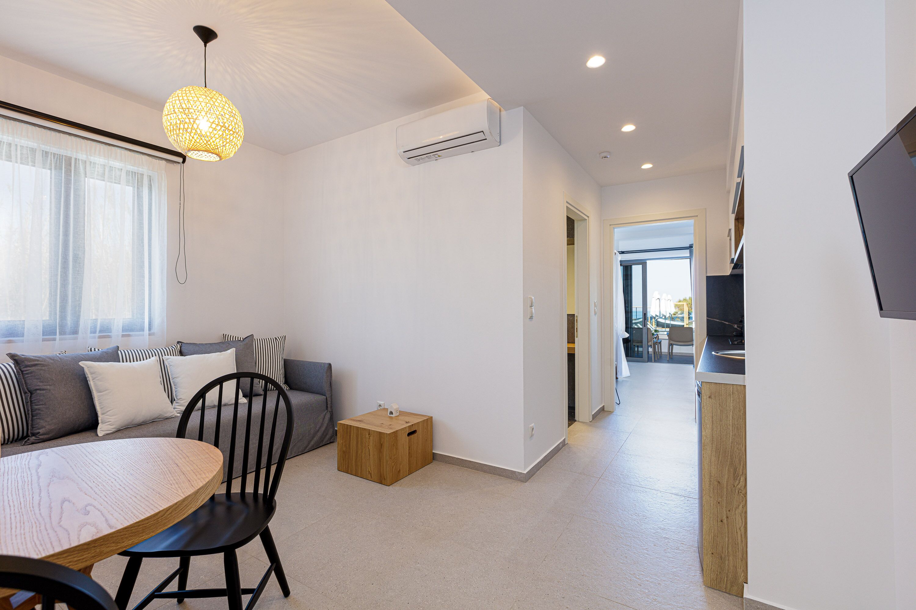 Una sala de estar moderna con una mesa redonda de comedor, un sofá con cojines, una mesita de madera y una lámpara colgante.