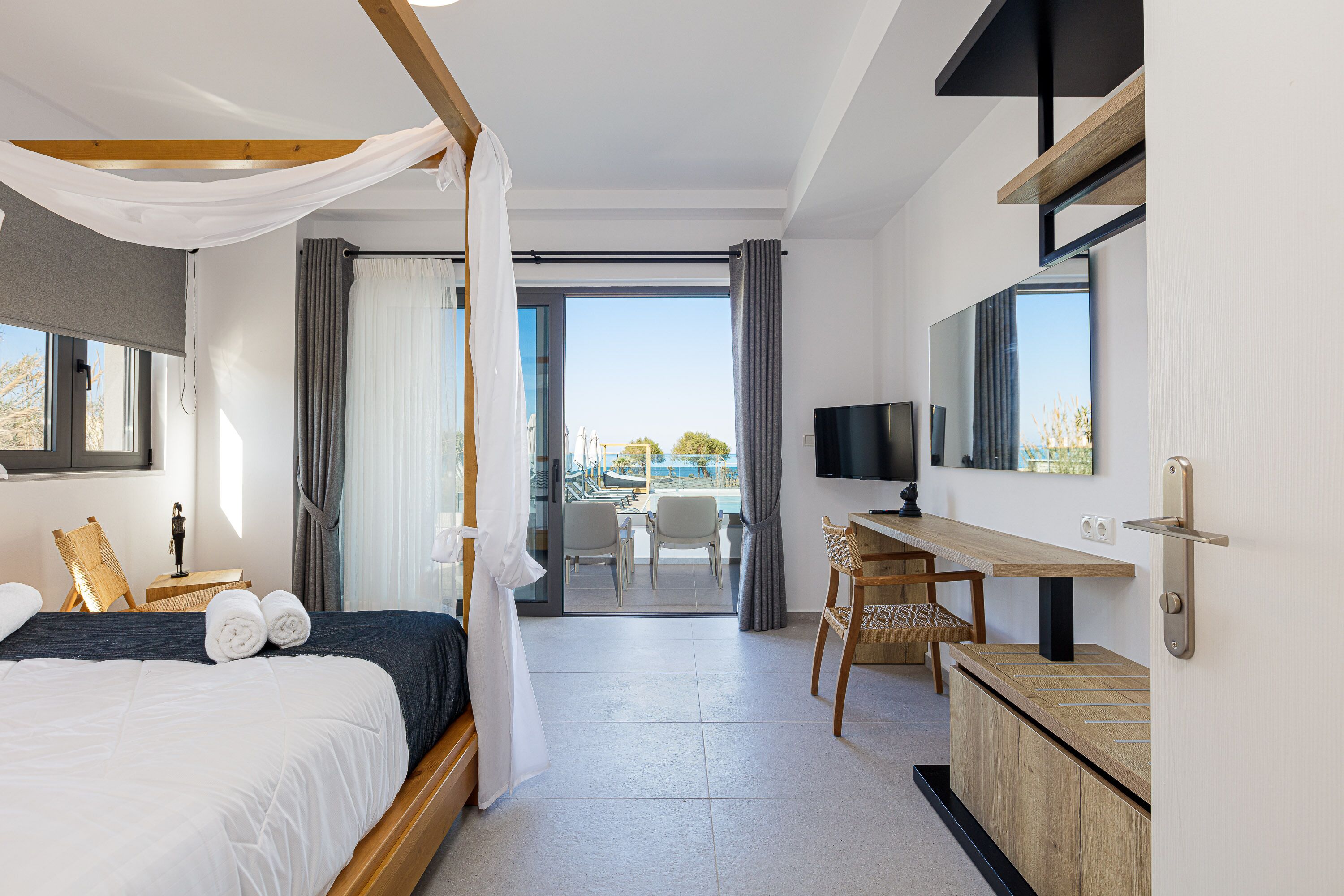 A modern hotel room with a large bed, a desk, a television, and a balcony with a view.