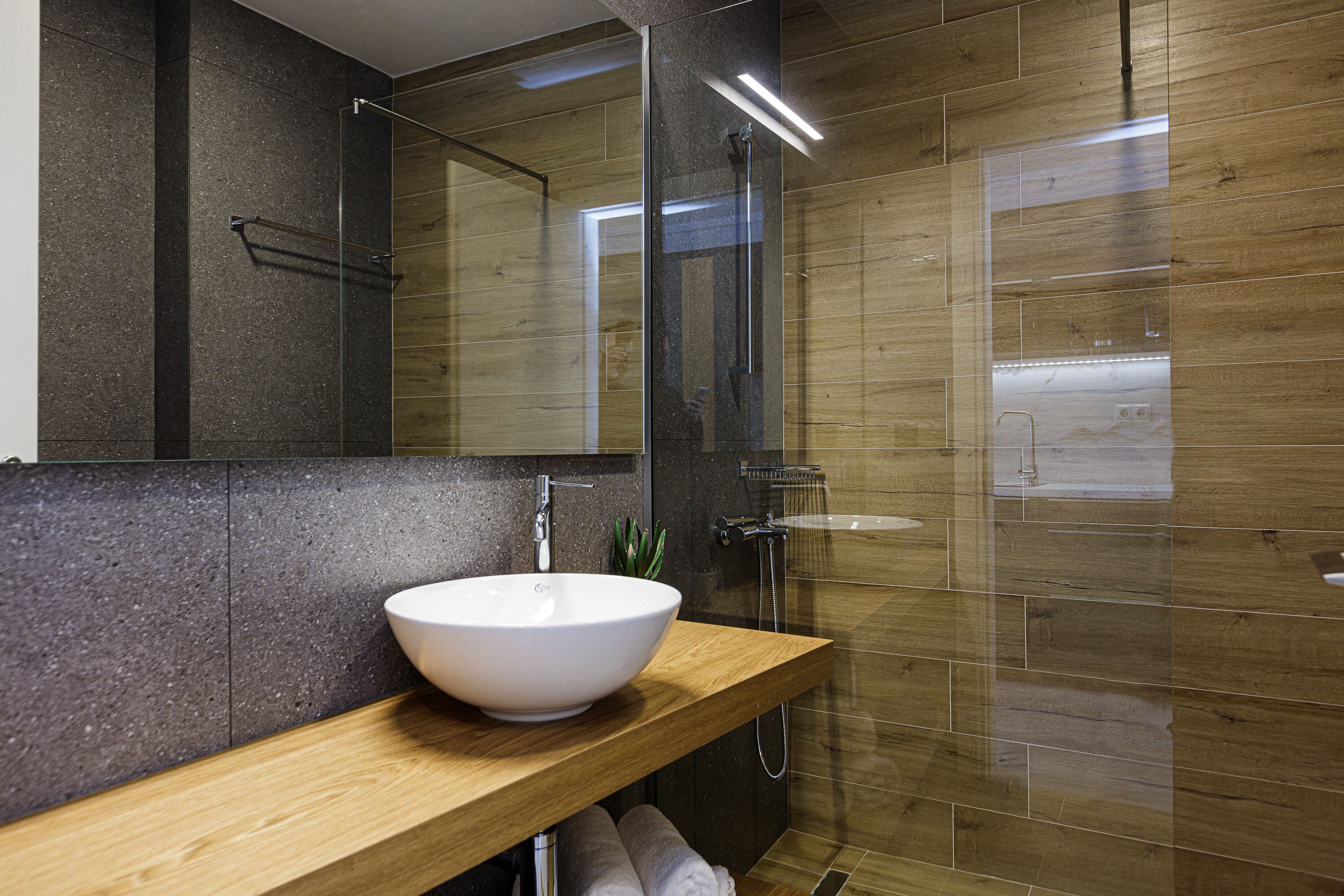 A modern bathroom with a wooden vanity, a white vessel sink, a glass-enclosed shower, and a mirror.