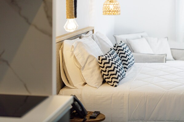 A neatly made bed with white and patterned pillows, a bedside table with a phone and remote, and a hanging light fixture. - Eleven Boutique Suites (Rethymno)