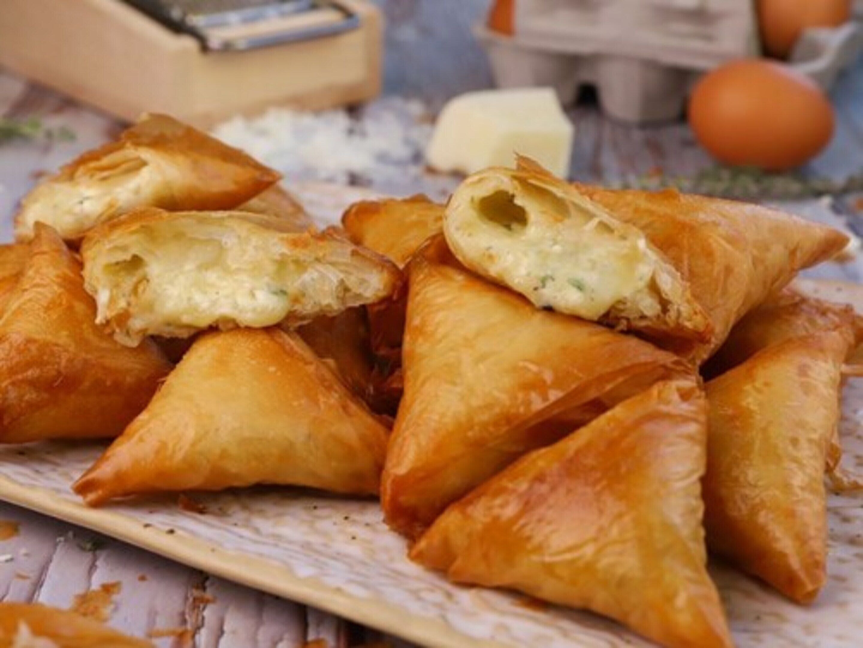 A plate of golden-brown pastries, likely samosas, with one cut open to reveal a creamy filling.