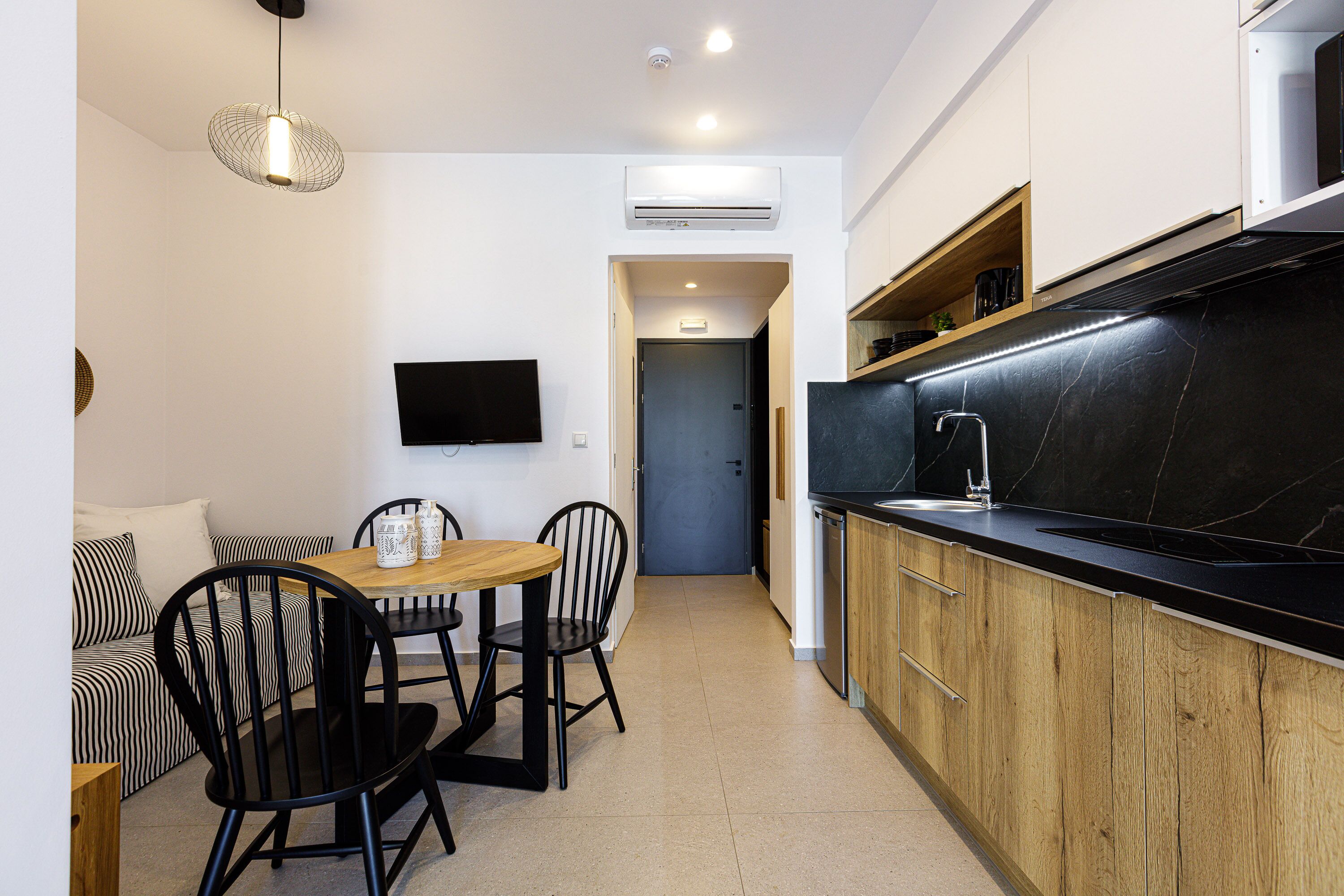 A compact kitchen with a black countertop, wooden cabinets, and a dining area with a table and chairs.