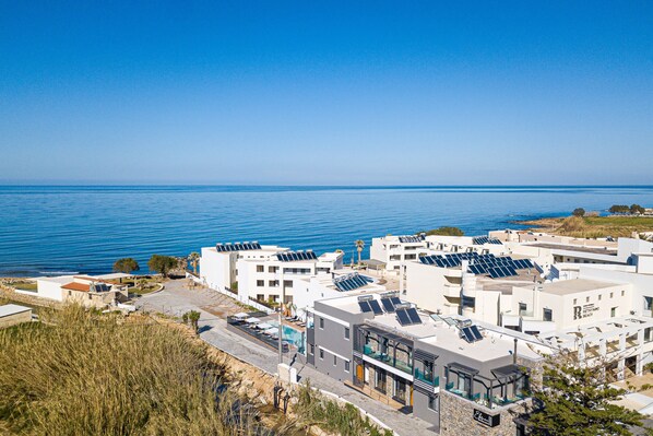 Un hotel costero con varias edificaciones, paneles solares en los tejados y una vista despejada del mar.
