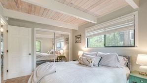 Une chambre à coucher avec un grand lit, un miroir, une fenêtre avec des stores et une table de chevet avec une lampe.