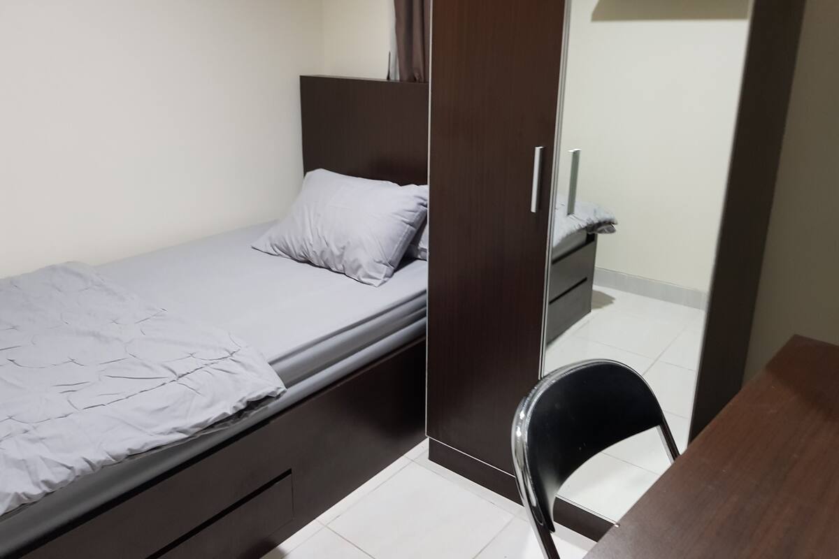 A small, neatly arranged bedroom with a single bed, a wardrobe, and a chair.