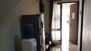 A corridor with a water dispenser, a refrigerator, and a fan on a table. - Aloha Guest House 2 (Gading Serpong)