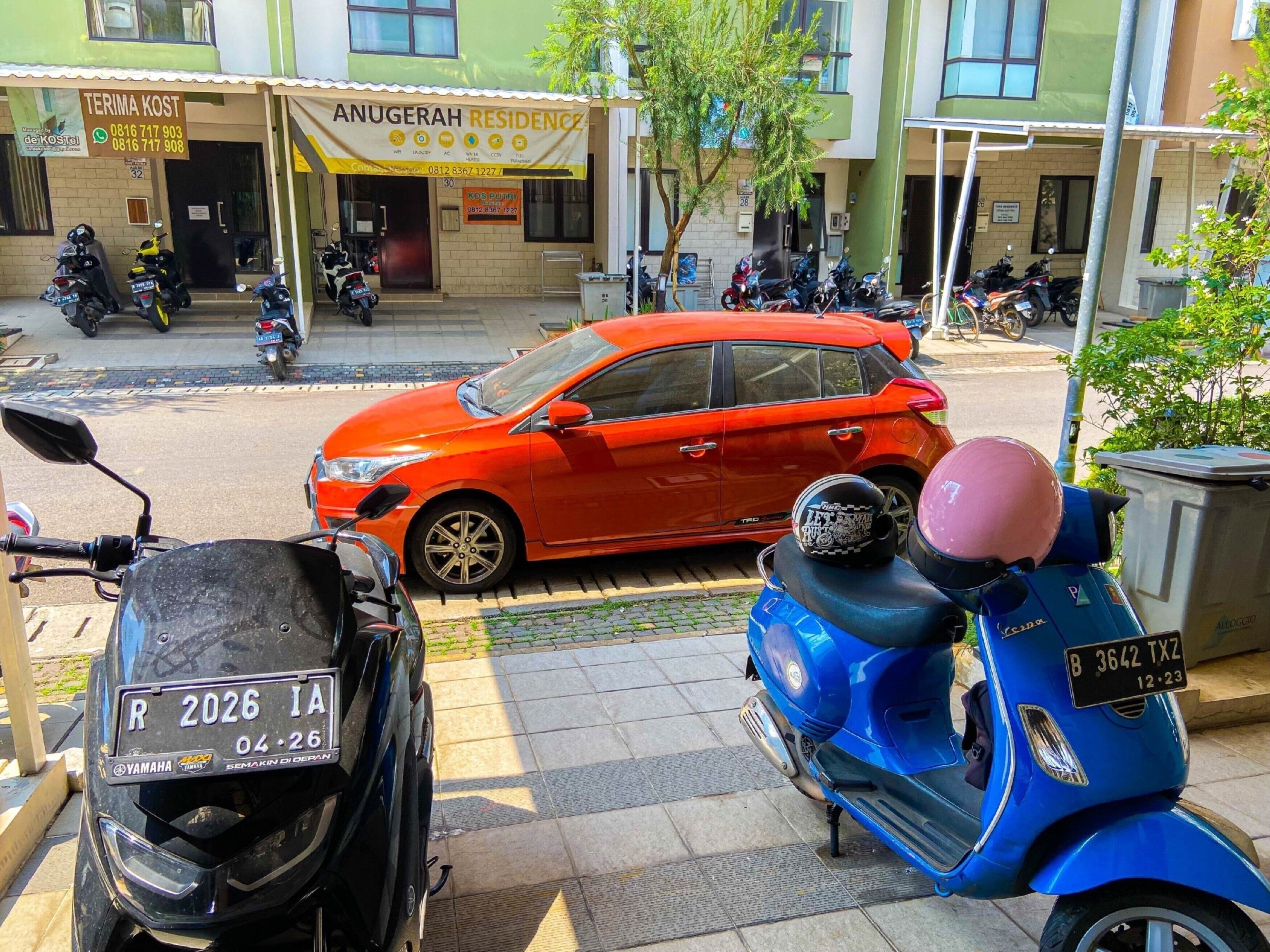 Une voiture rouge est garée dans une rue, avec un scooter bleu en premier plan.