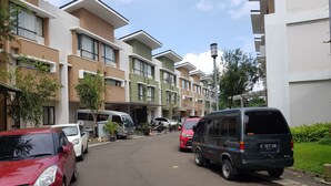 A residential street with modern apartment buildings, parked cars, and a shuttle bus. - Aloha Guest House 2 (Gading Serpong)