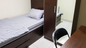 A small, single-bed room with a wooden wardrobe, a bedside table, and a chair. - Aloha Guest House 2 (Gading Serpong)