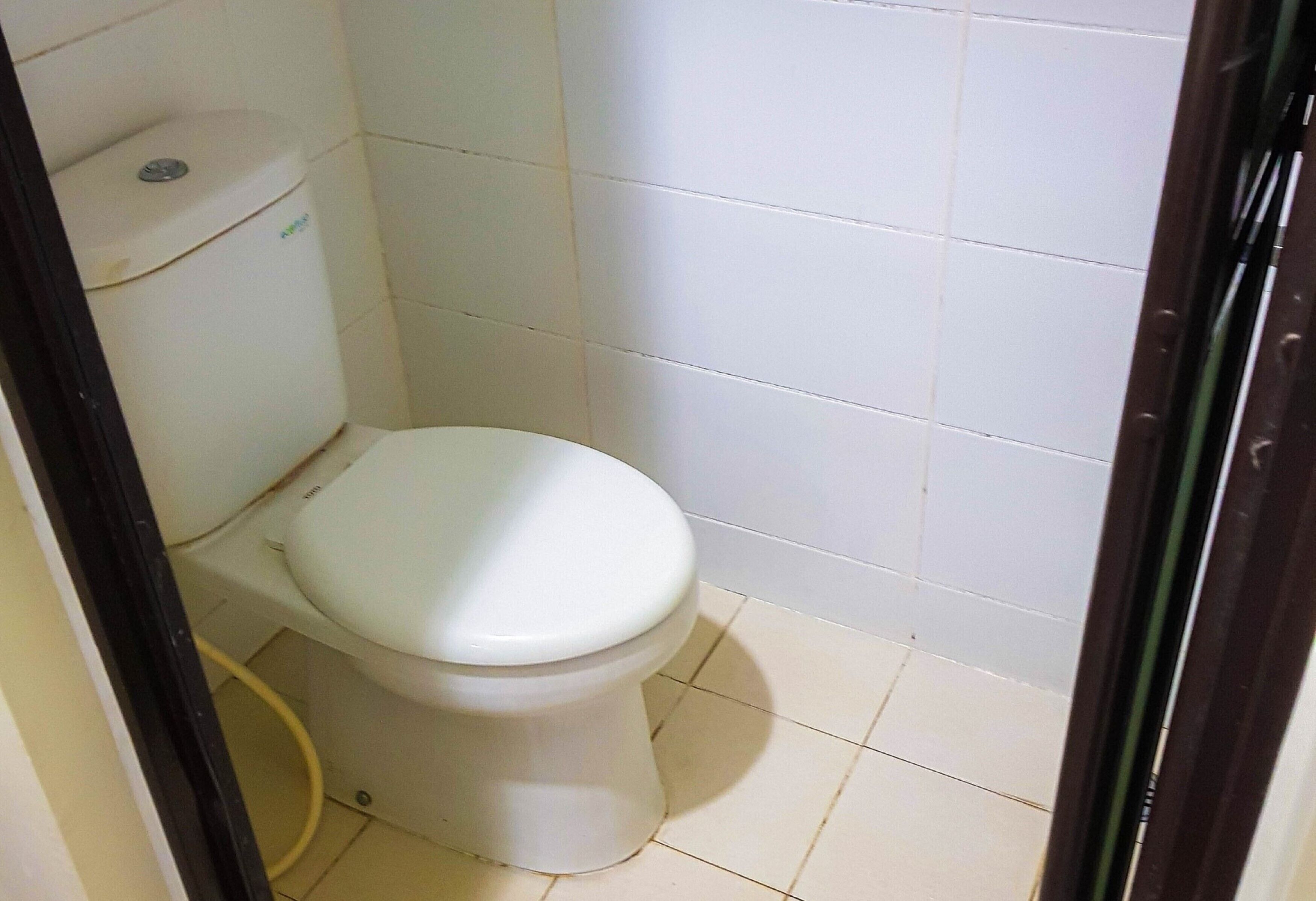 Pieni, valkoinen wc-istuin kylpyhuoneessa, jonka seinät ja lattia ovat valkoisilla laatoilla.