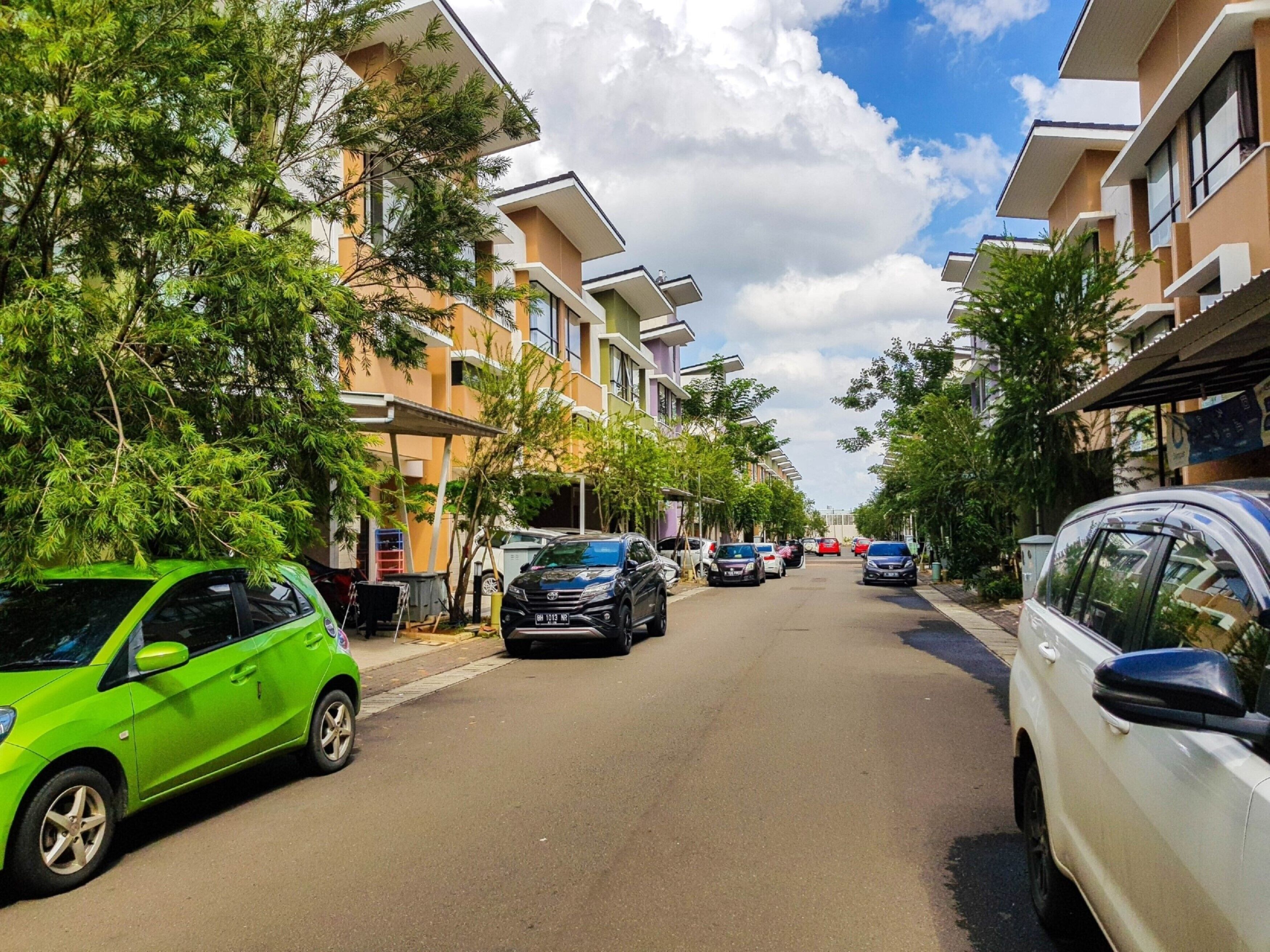 En boligbelagt gade med moderne lejlighedskomplekser, parkerede biler og frodig beplantning.