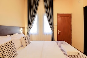 Una habitación de hotel con una cama bien hecha, una puerta de madera y un ventanal con cortinas.
