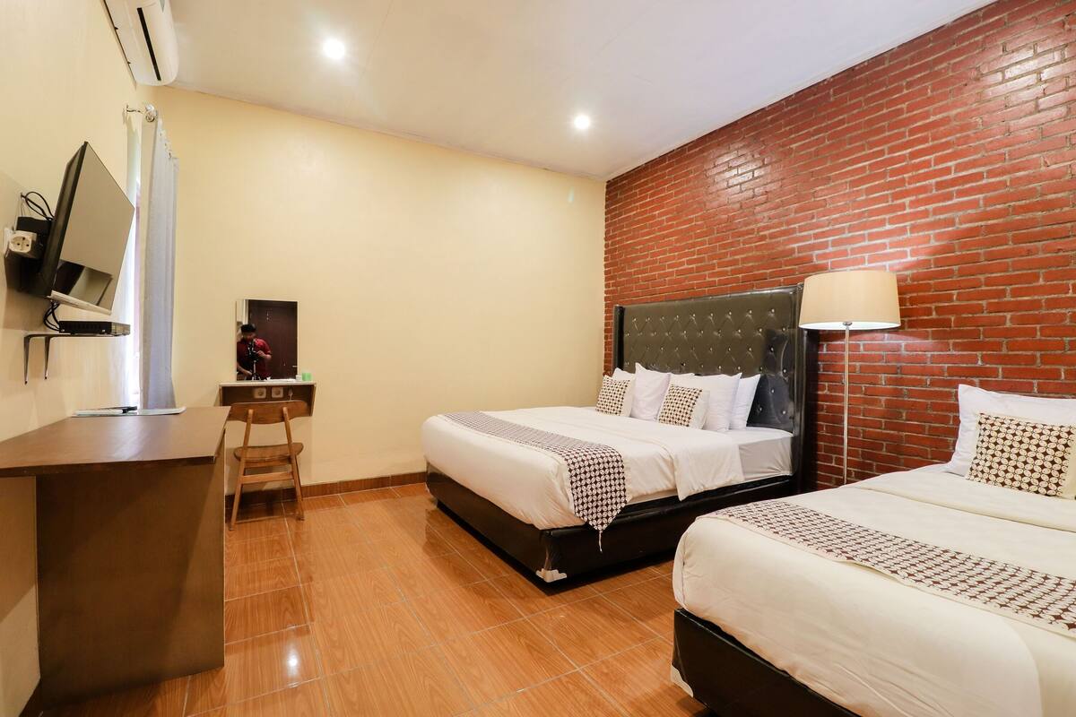 A hotel room with two beds, a desk, and a mirror.