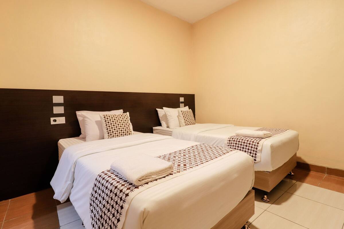 A hotel room with two beds, each with white bedding and patterned throw pillows.