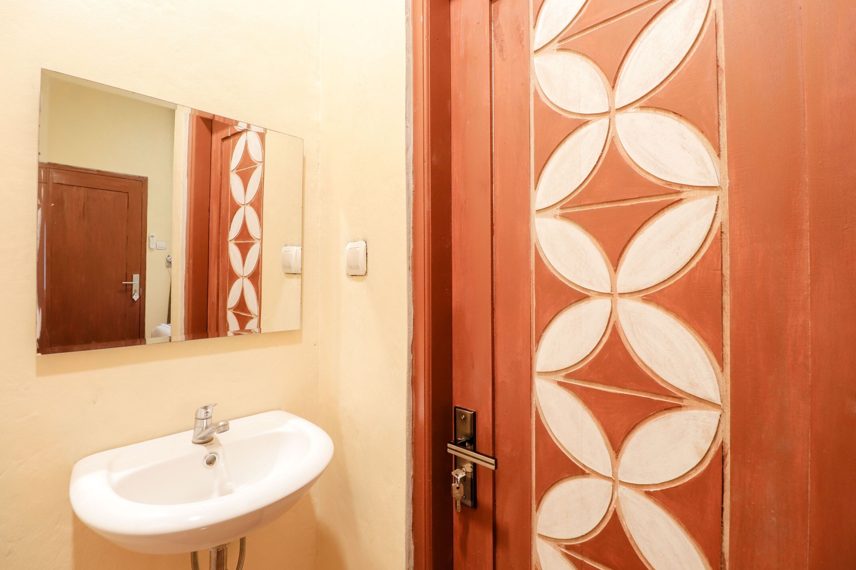 A bathroom with a white sink, a mirror, and a wooden door with a geometric pattern.