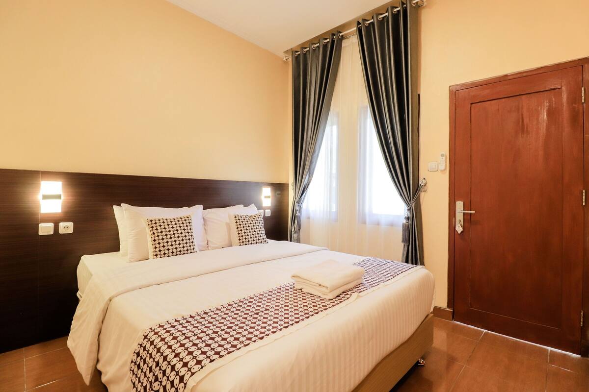 A hotel room with a large bed, a wooden door, and a nightstand with a lamp.