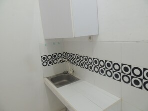 A small kitchen with white cabinets, a stainless steel sink, and a patterned backsplash. - Kozi Kost Paviliun (Tegal)