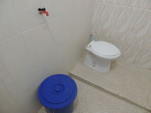 A bathroom with a toilet, a blue trash bin, and a wall-mounted faucet. - Kozi Kost Paviliun (Tegal)