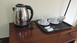 A wooden table with a stainless steel electric kettle, two white cups, saucers, a glass, and a tray with rolled towels. - Srikayah by Ndalem Beong (Borobudur)
