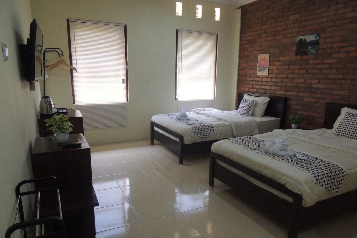 Quarto de hotel com duas camas, uma mesa, uma cadeira e um vaso de planta.