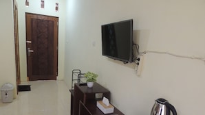 A hotel room with a wooden desk, a television mounted on the wall, a kettle, and a small table with a plant and a tissue box. - Srikayah by Ndalem Beong (Borobudur)