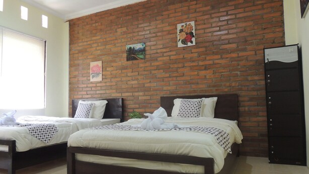 A hotel room with two beds, a brick wall, and a door. - Srikayah by Ndalem Beong (Borobudur)
