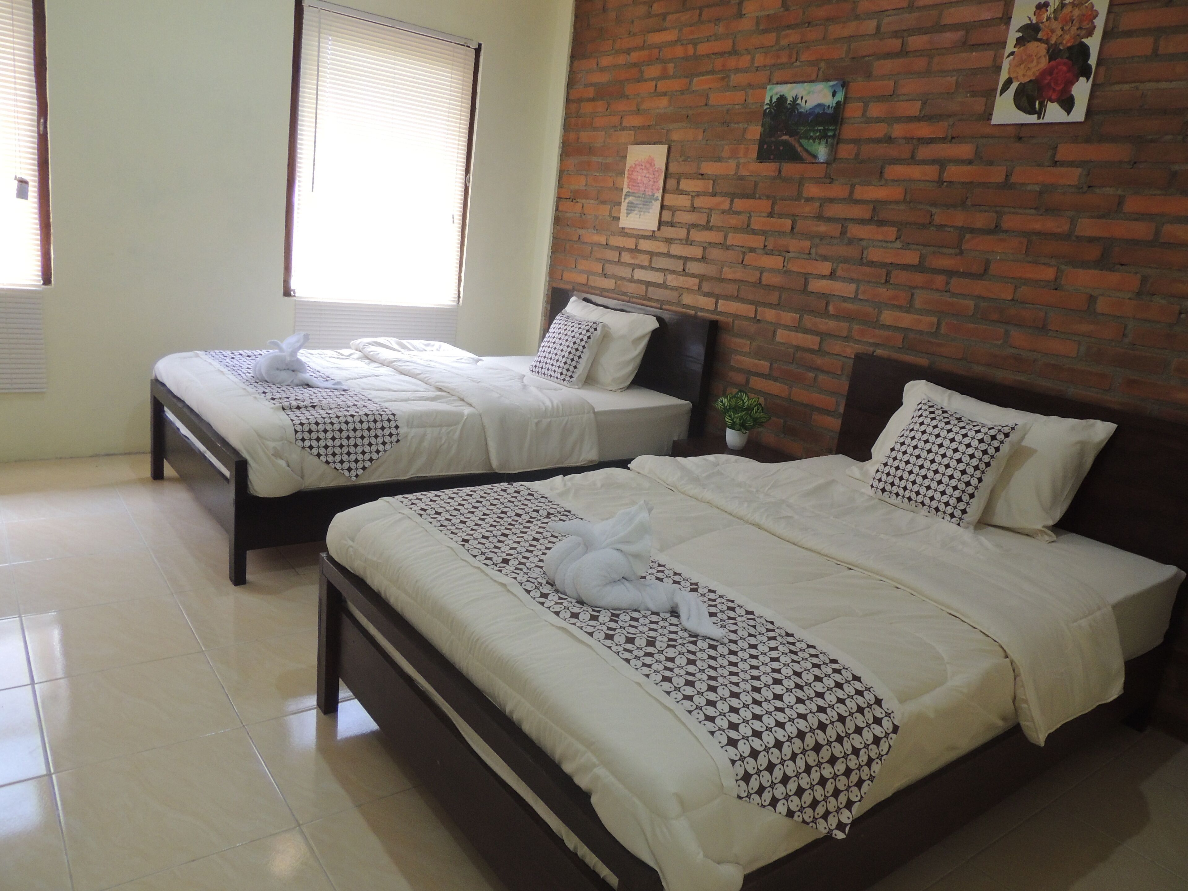 A hotel room with two beds, a brick wall, and a window.