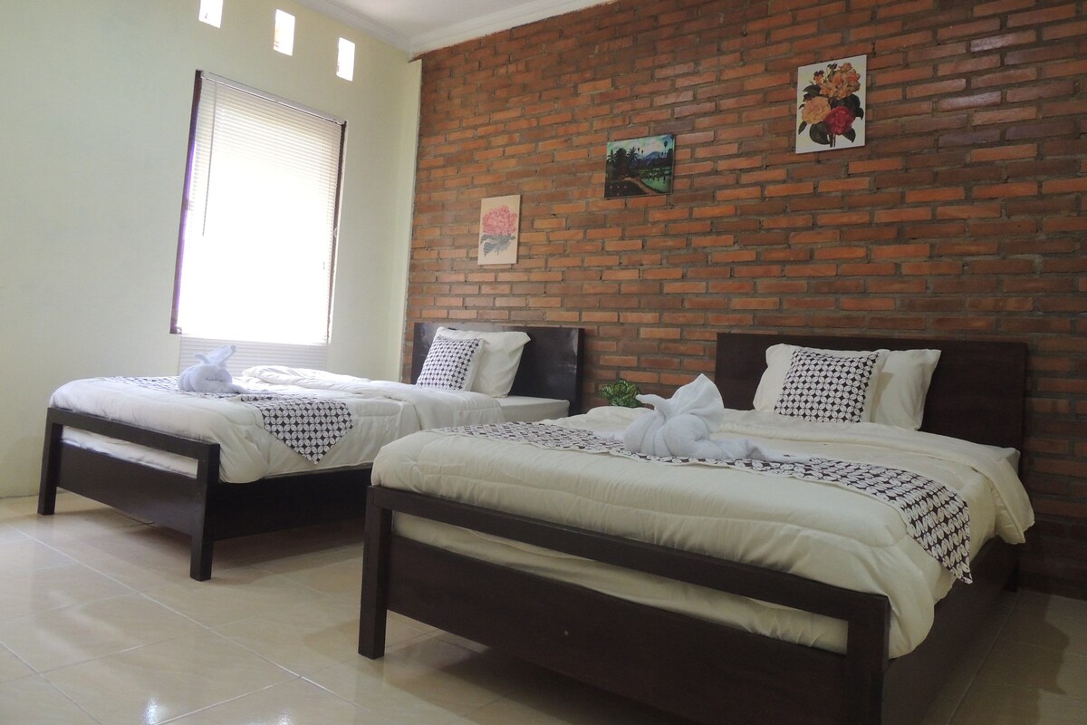 Two single beds with dark wooden frames and white bedding, a brick wall, and a window with blinds.