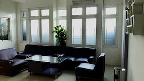 A modern living room with a black leather sofa, a glass coffee table, and large windows providing natural light.