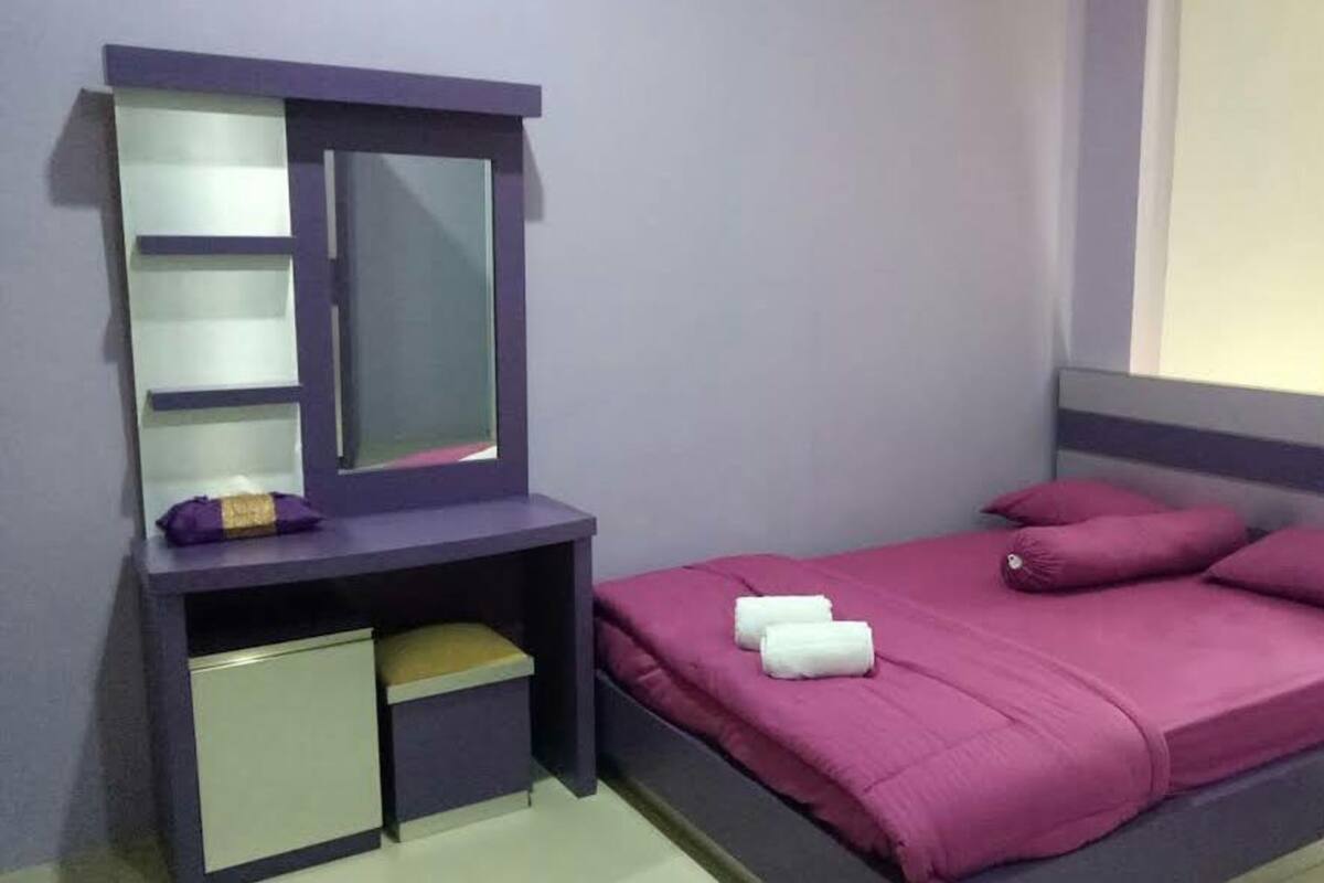 Ein Schlafzimmer mit Bett, Nachttisch, Kommode, Spiegel und einem Fenster mit Vorhängen.