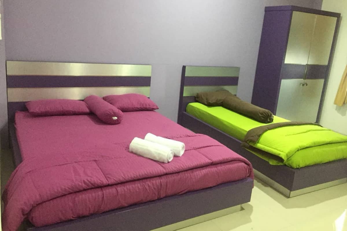 Ein Zimmer mit zwei Betten, eines mit einer violetten Tagesdecke und das andere mit einer grünen Tagesdecke. Es gibt einen Kleiderschrank mit Spiegel und Tür.