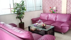 A living room with a pink sofa set, a glass coffee table with decorative items, a potted plant, and a patterned wallpaper.