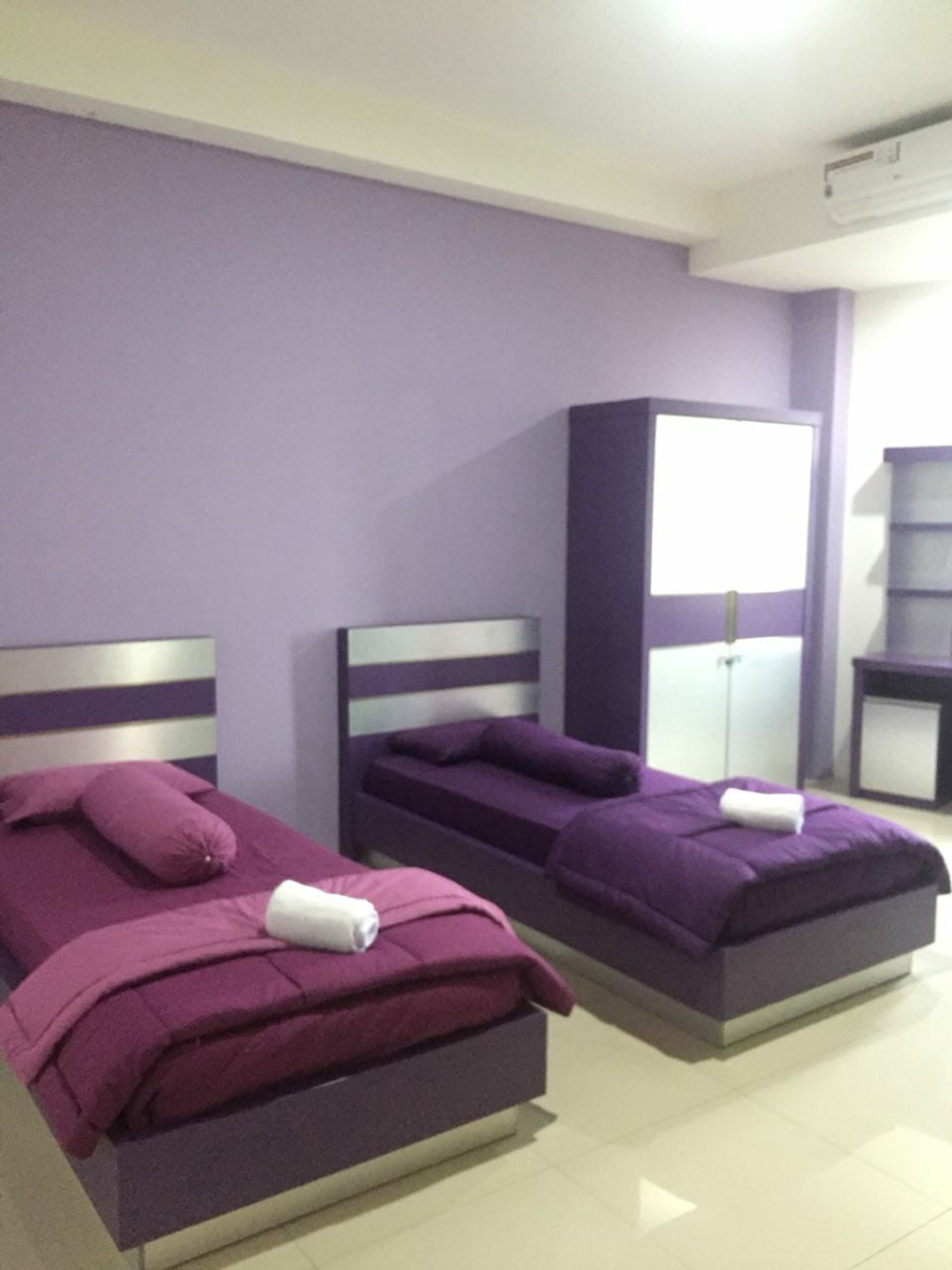 Zwei Betten mit violetter Bettwäsche und weißen Kopfteilen in einem Raum mit violetten Wänden und einer weißen Decke.