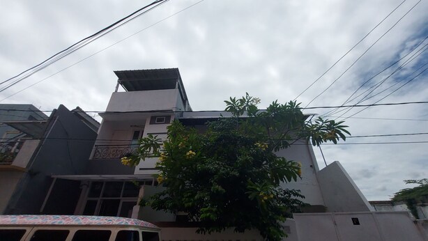 A building with a white facade, a balcony, and a tree with yellow flowers. - Eiffel Residence Cideng - Female Only (Jakarta)