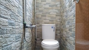 A small bathroom with a toilet, a shower, and a wall with a stone-like pattern. - Eiffel Residence Cideng - Female Only (Jakarta)