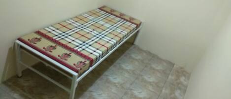 A small, single-bed room with a checkered bedspread and a simple, unadorned wall.