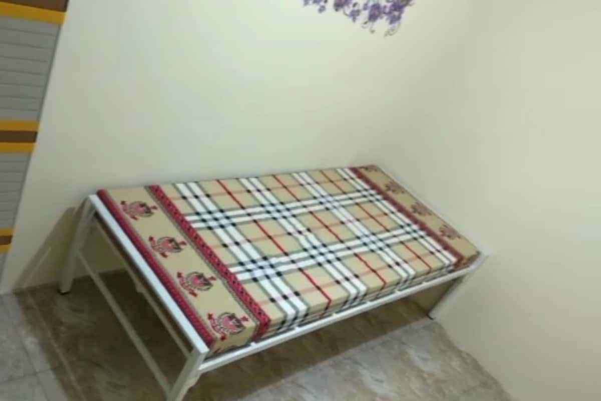 A small, white metal bench with a plaid cushion against a wall.