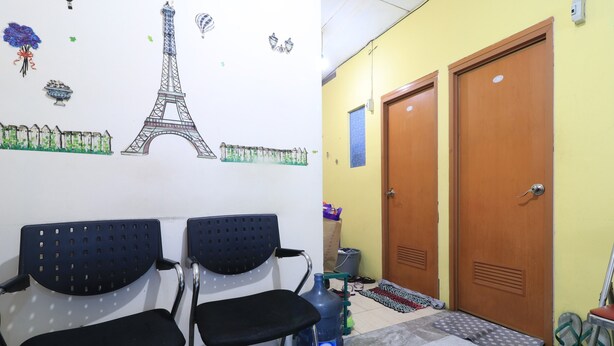 Ein Wartebereich mit zwei schwarzen Stühlen, einem großen Wasserspender und einer Wand mit Paris-Motiven, darunter der Eiffelturm und ein Gartenzaun.