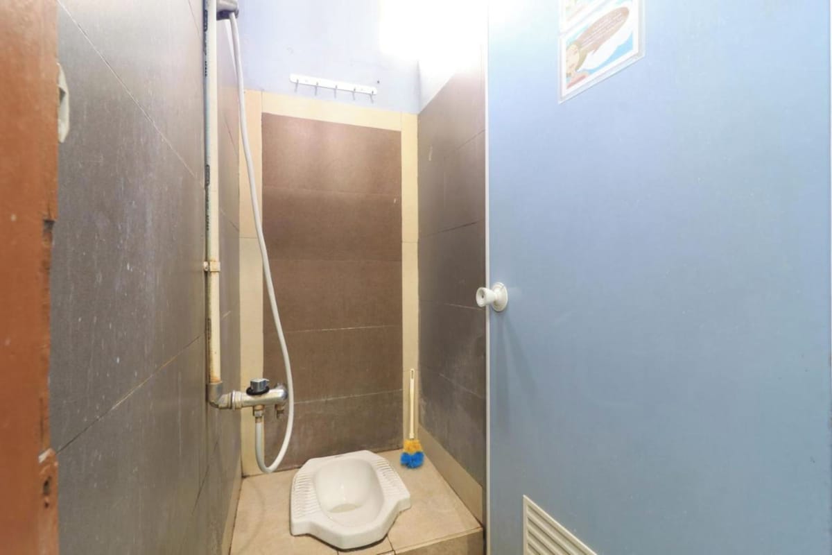 Une petite salle de bain étroite, avec des toilettes à la turque, un espace douche et un balai.