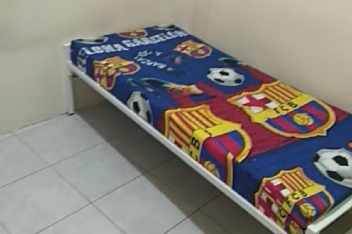 Una habitación pequeña y estrecha con una cama individual cubierta por un edredón con motivos deportivos.