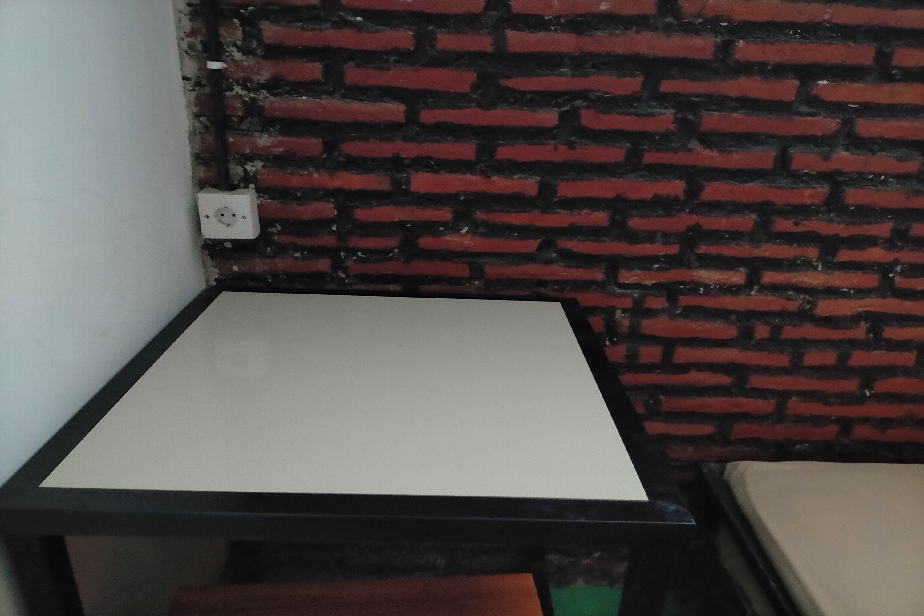 Eine Ecke eines Raumes mit einem weißen Tisch und einer Ziegelwand.